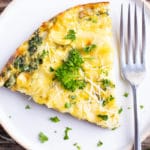 A slice of spinach artichoke crustless quiche on a white plate with a fork.