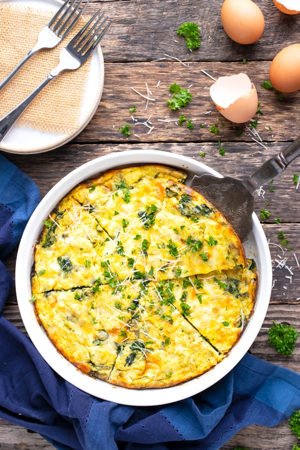 Spinach quiche breakfast recipe with eggs in a white pie plate on a wooden backdrop.