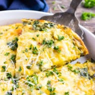 A slice of an egg bake recipe with spinach and cheese being picked up out of a casserole dish.