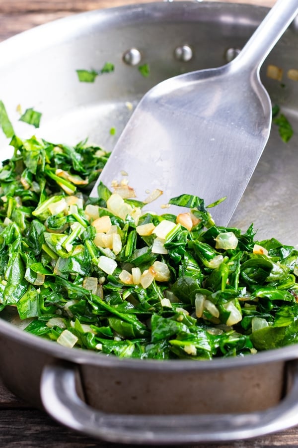 Sauteed fresh spinach and onions in a stainless steel pan.
