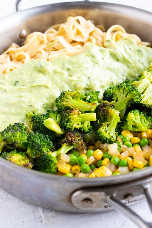 Avocado Pesto Pasta with broccoli, peas, and corn in a steel skillet.