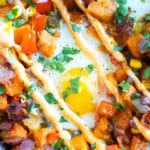 An egg in the middle of a sweet potato hash with sriracha mayo and cilantro on top.