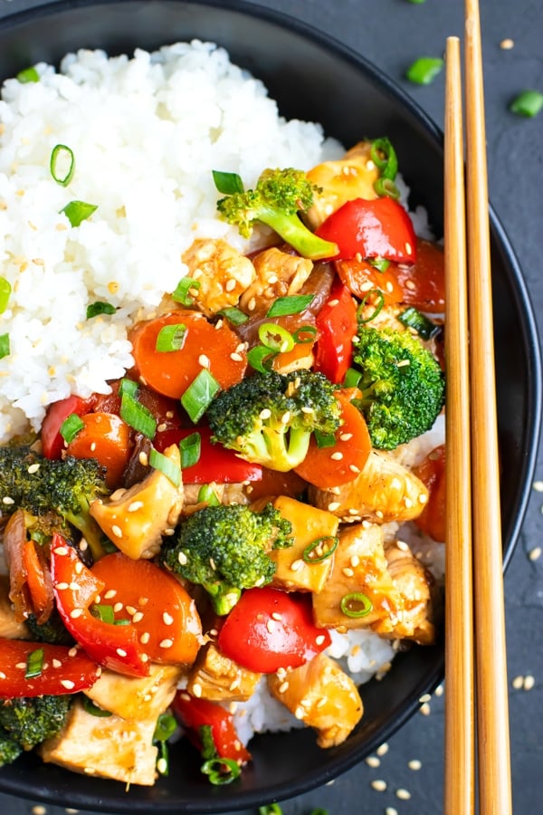 A black bowl full of a teriyaki chicken recipe with wooden chopsticks.