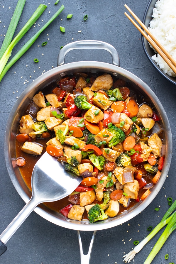 Teriyaki chicken stir fry in a stainless steel skillet with a spatula.