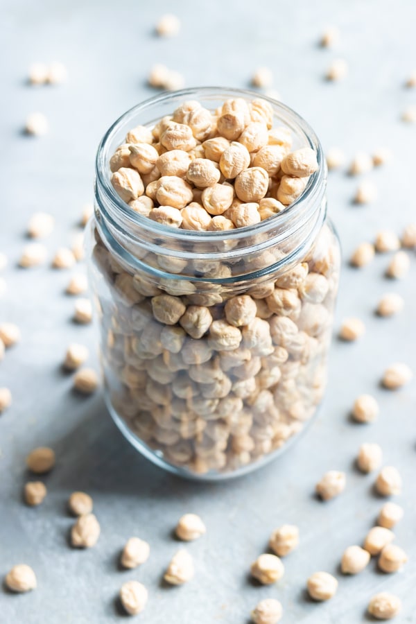 Dried chickpeas in a clear glass jar with a lot of chickpeas around it.
