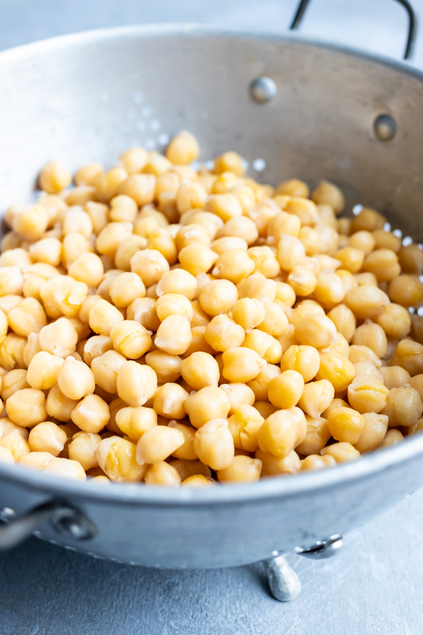 A silver strainer full of cooked chickpeas that have been thoroughly drained.