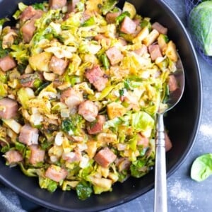 A black bowl full of shaved Brussels sprouts, cubed ham, and mustard sauce.