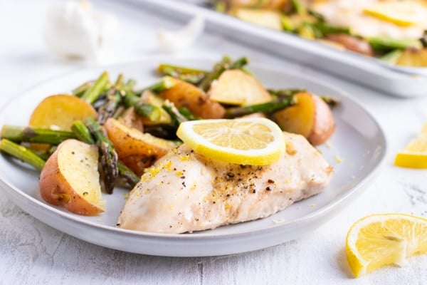 A white plate full of healthy lemon chicken with roasted potatoes and asparagus.
