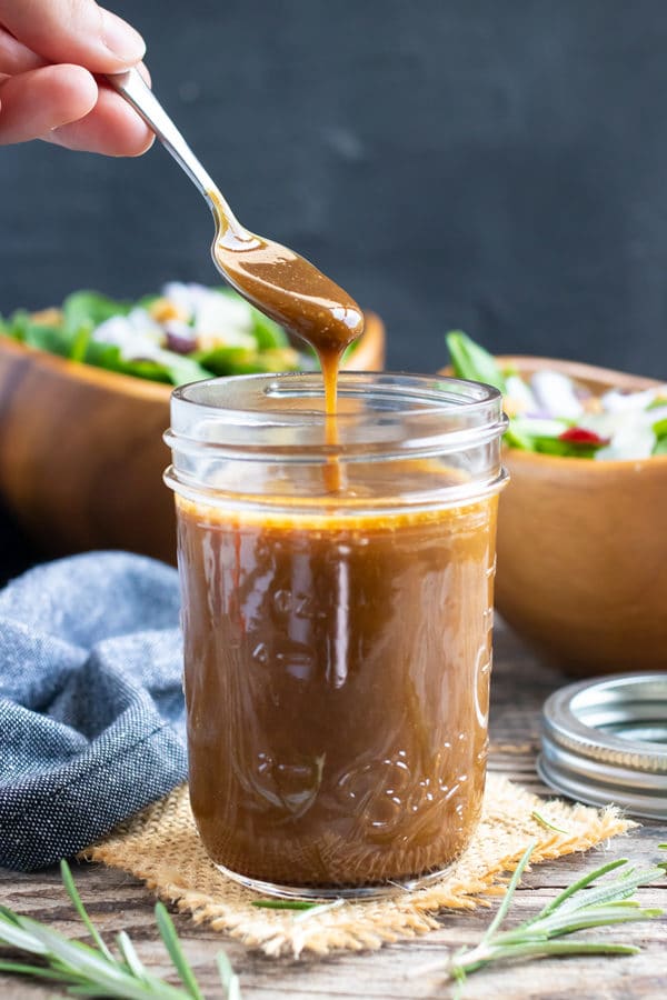 A mason jar full of balsamic and maple syrup salad dressing with two salads in the background.