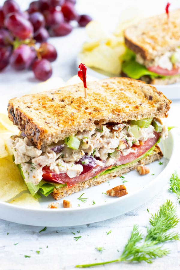 Chicken salad sandwich with a red toothpick on a white plate with potato chips.