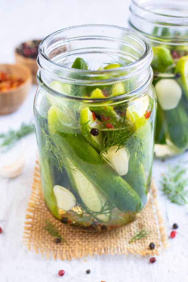 Refrigerator pickles in a glass jar with dill sprigs, red pepper flakes, and garlic cloves.