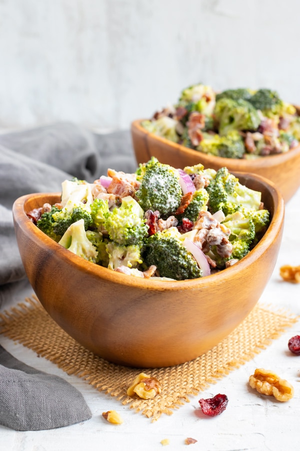 Two salad bowls full of a cold broccoli salad recipe with walnuts, cranberries, and bacon.