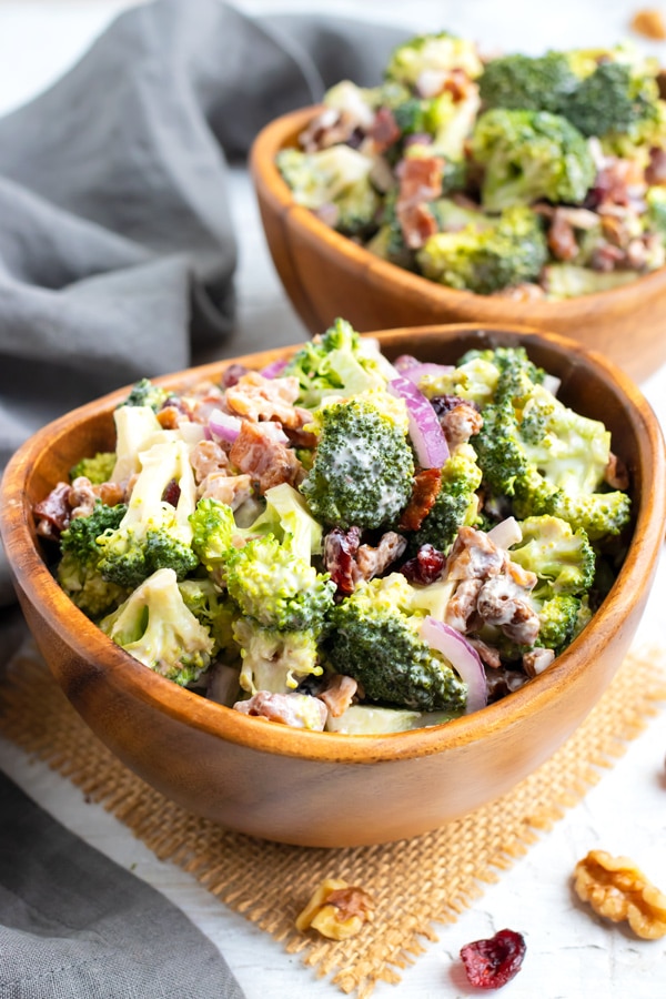 A wooden serving bowl full of a cold broccoli salad recipe with walnuts, cranberries, and bacon.