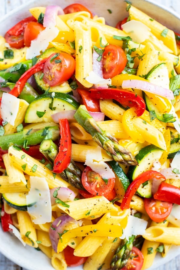 A large white bowl full of a vegetable pasta recipe with tomatoes, asparagus, and bell peppers.