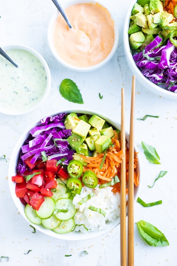 Two Vegan Sushi Bowls with two small bowls of sriracha mayo and wasabi cilantro sauce.