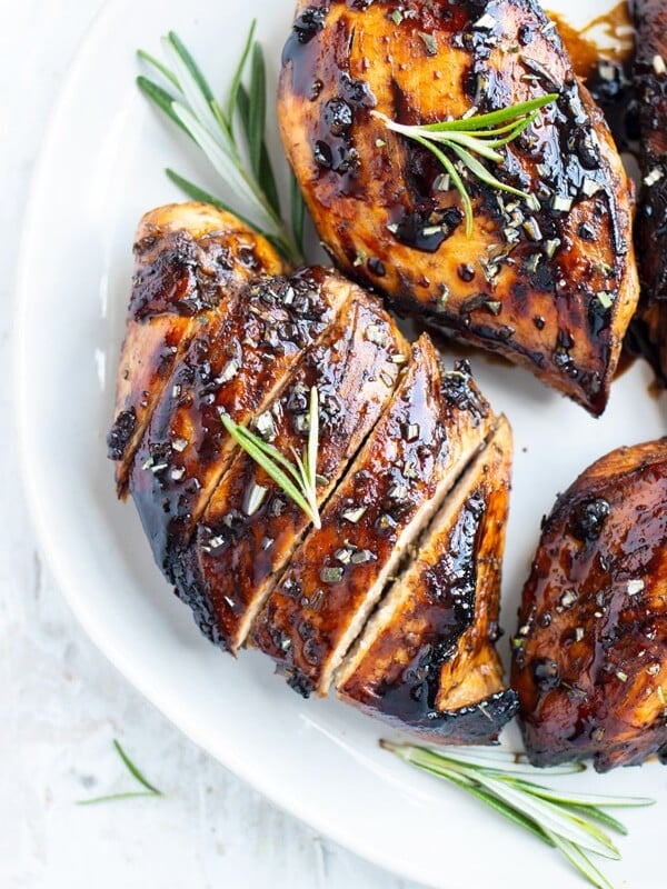 A honey balsamic chicken breast on a white plate with a sprig or rosemary.