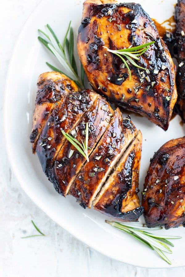 A honey balsamic chicken breast on a white plate with a sprig or rosemary.