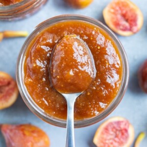 A silver spoon scooping out a serving of homemade fig jam from a glass mason jar.