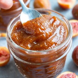 A spoon scooping out a tablespoon of a fig jam recipe from a glass jar.