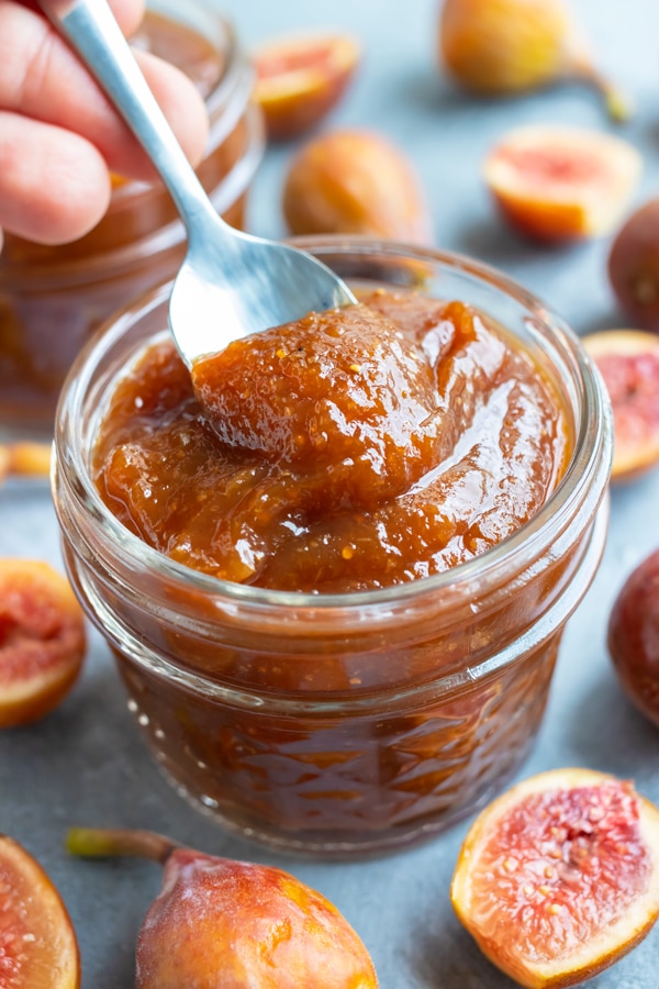 A spoon scooping out a tablespoon of a fig jam recipe from a glass jar.