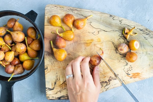 Cutting the stems off of brown turkey figs on a wooden cutting board for a fresh fig recipe.