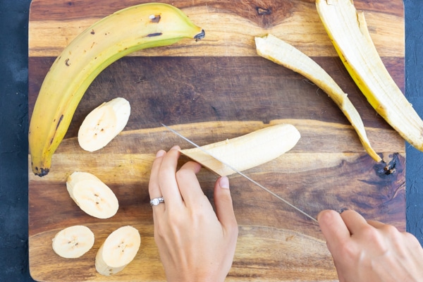 A hand cutting plantains with a knife to show how to cut ripe plantains for a fried plantains recipe.