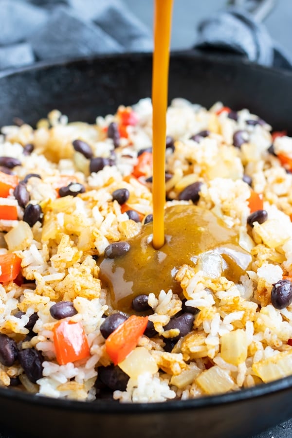 Lizano sauce being poured into a skillet full of rice and black beans.