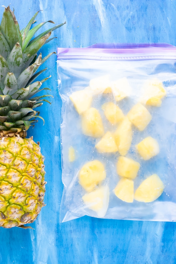 A pineapple next to a bag of frozen fresh pineapple for a pina colada recipe.