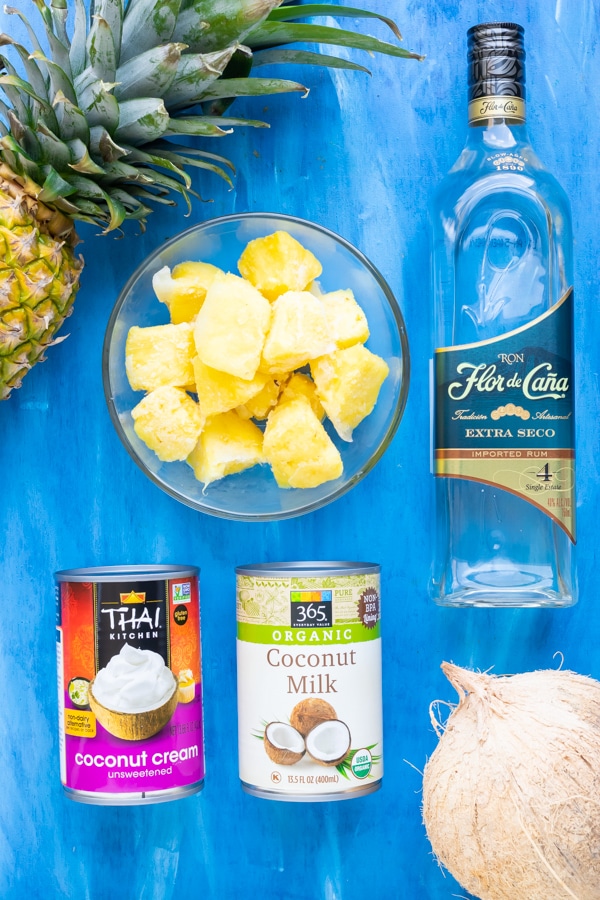 Fresh pineapple, coconut milk, coconut cream, and white rum as the ingredients in a pina colada recipe.