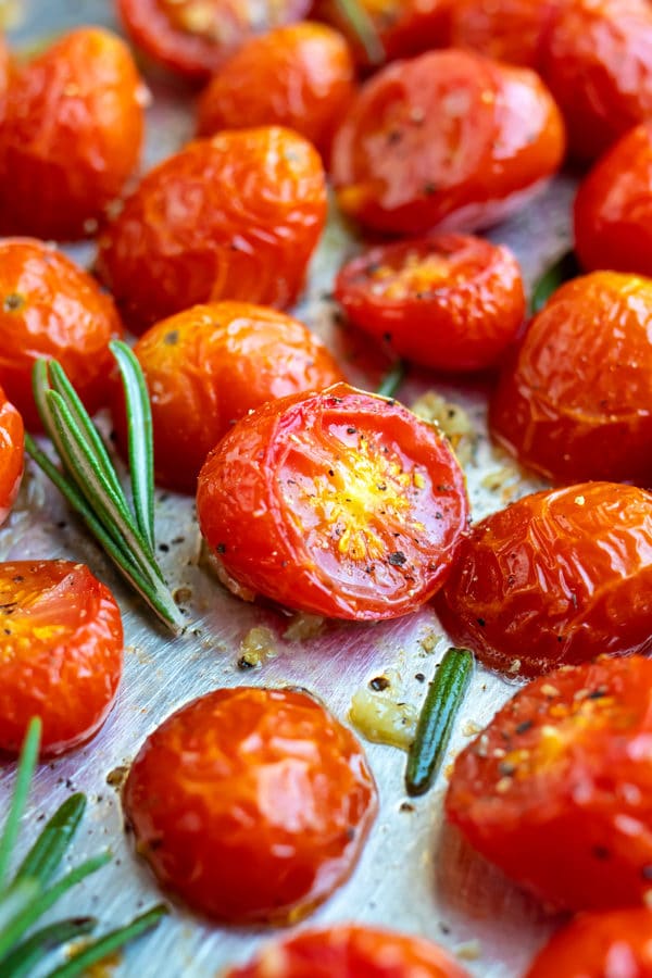 Roasted cherry tomatoes on a baking sheet with rosemary next to it.