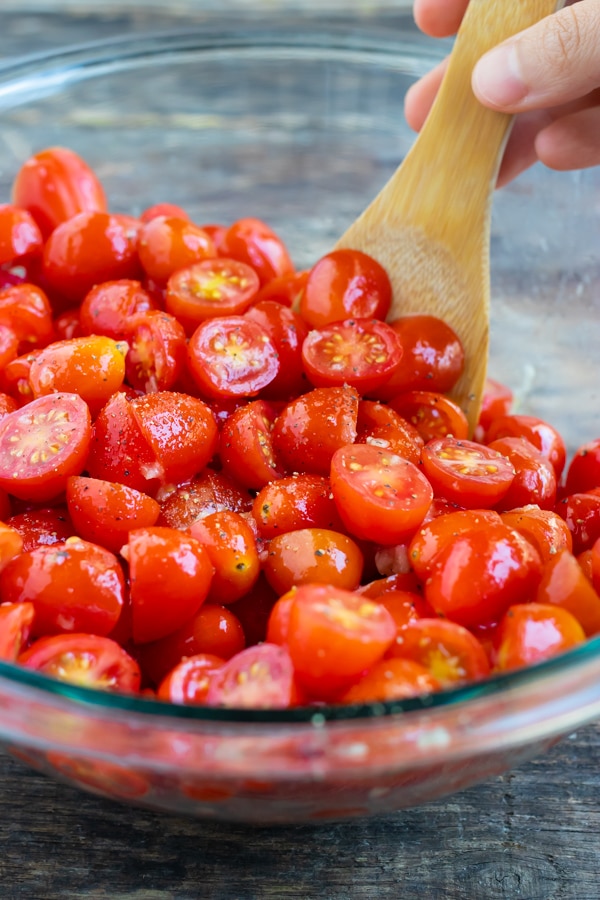Cherry tomatoes being tossed in garlic and olive oil before being roasted in the oven.
