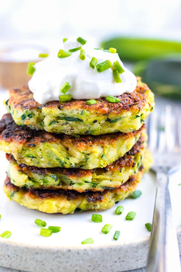 A stack of fried zucchini fritters with sour cream on top.
