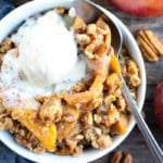 A white bowl full of a baked apple recipe with a scoop of vanilla ice cream.