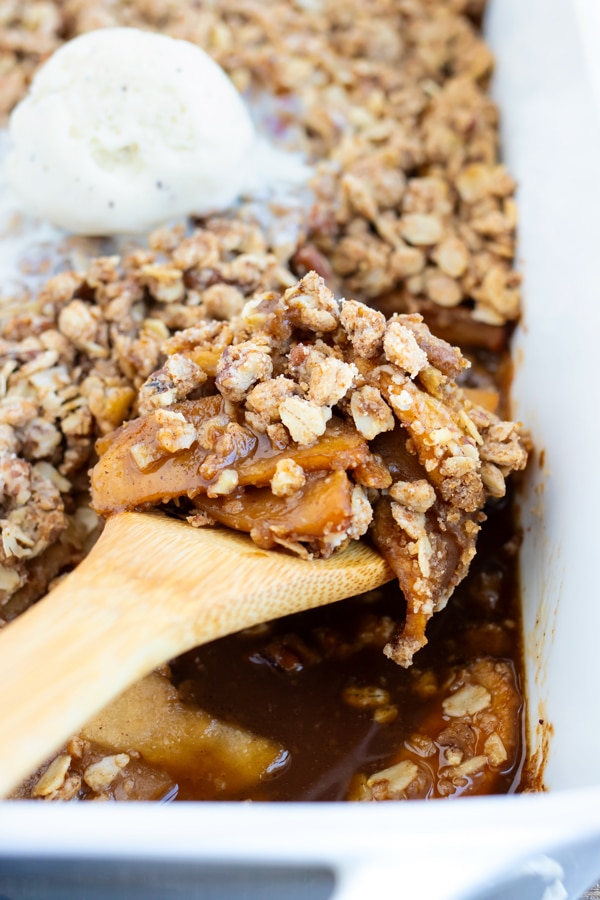 A wooden spoon scooping out a serving of a vegan apple crisp.