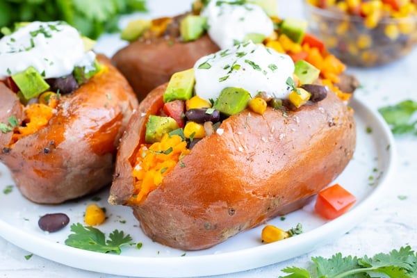 A loaded sweet potato with a Mexican taco filling of black beans, tomatoes, corn, and taco seasoning mix with sour cream on top.