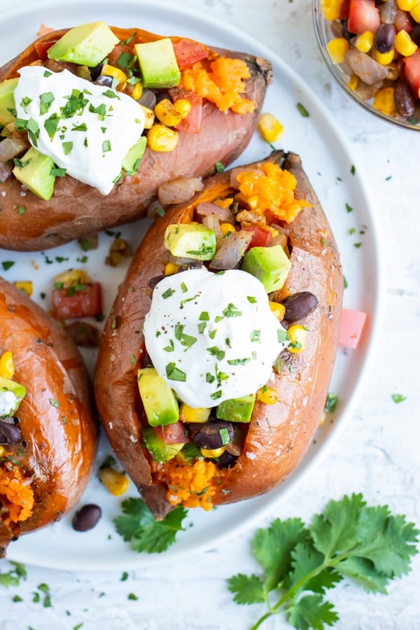 Mexican stuffed baked sweet potatoes on a white plate next to a bowl of corn and black beans.