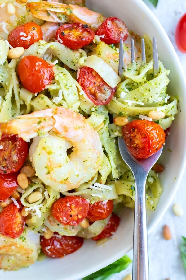Shrimp Pesto Pasta recipe in a white bowl with some of the pasta wrapped around a metal fork.