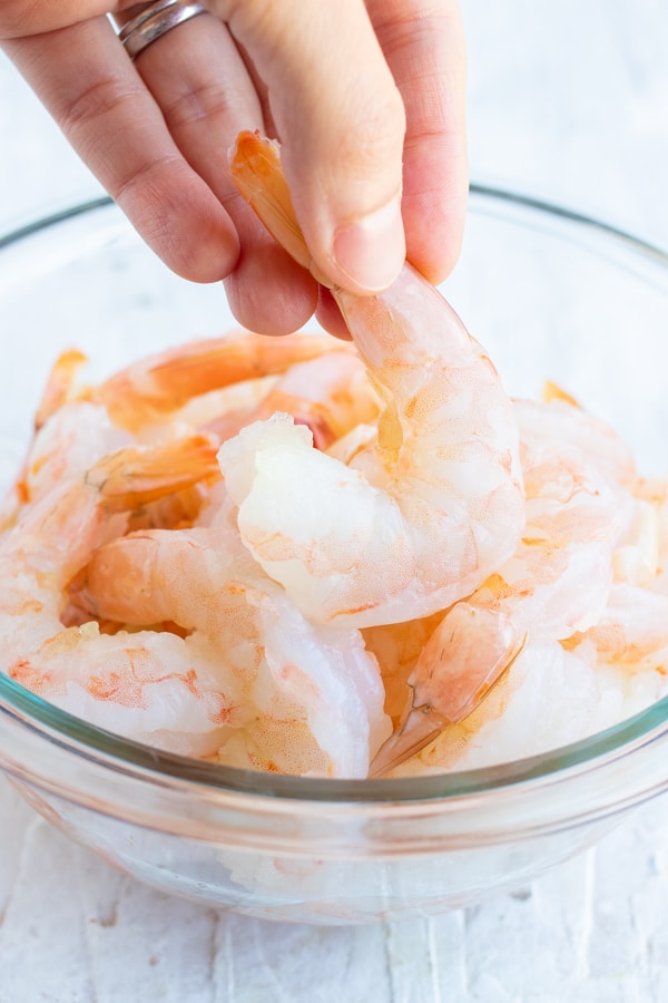 A hand holding a wild and fresh uncooked pink shrimp with the tail on.