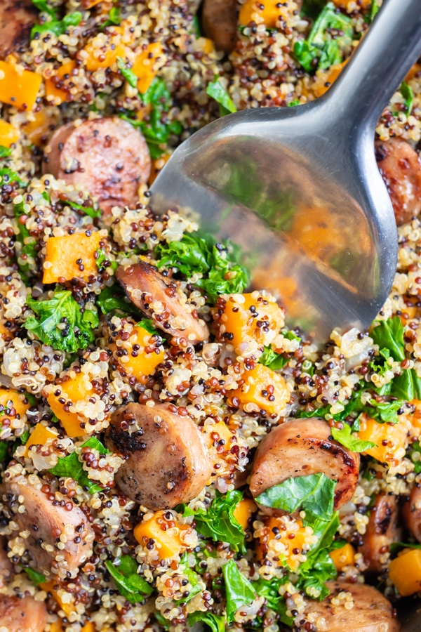 A silver spatula scooping out a quinoa and sweet potato recipe with sausage.