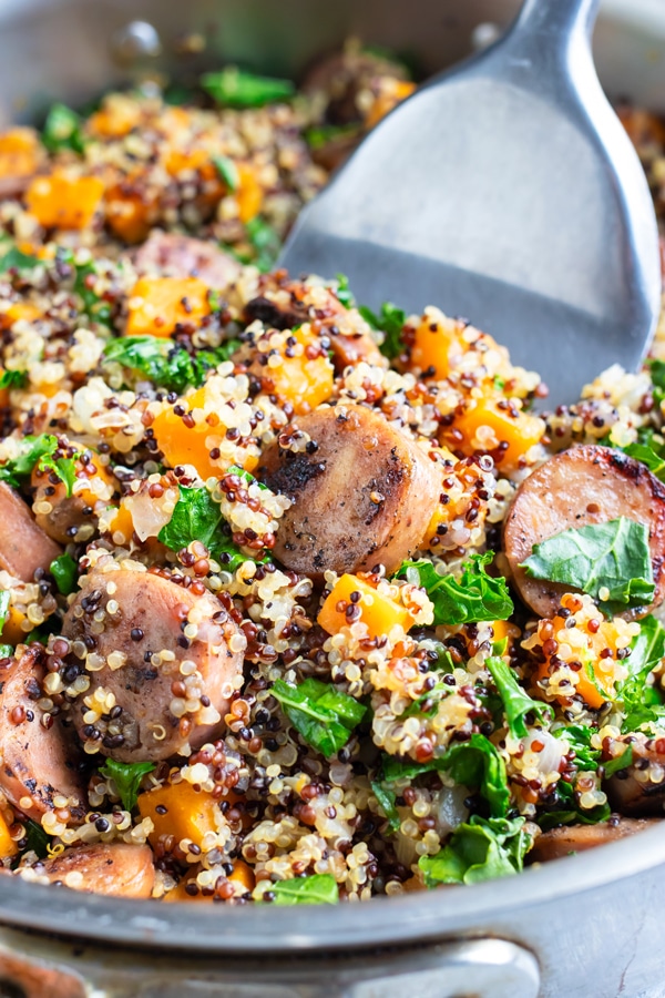 A silver spatula scooping out a quinoa and sweet potato recipe with sausage.