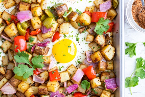 An over-easy egg in the middle of a pan full of roasted breakfast potatoes, bell peppers, and onions.