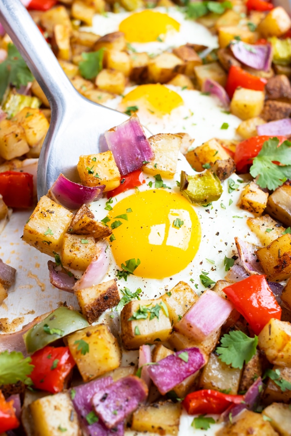 A metal spatula scooping out a serving of a breakfast potato hash and eggs recipe from a sheet pan.