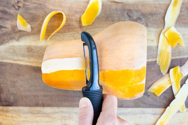 Peeling butternut squash with a vegetable peeler.