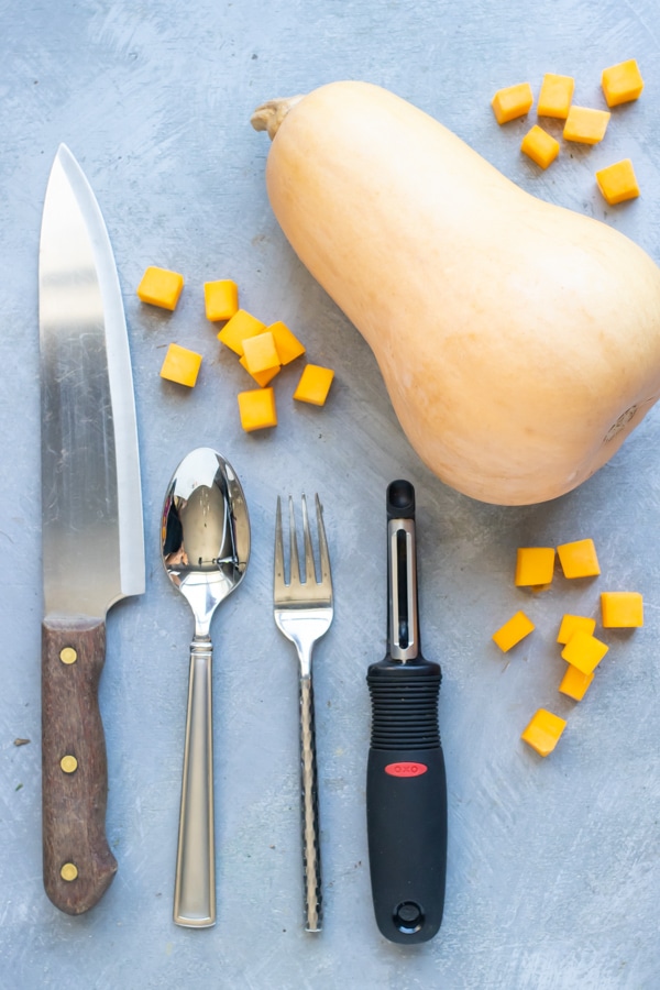 A knife, spoon, fork, and potato peeler to peel and cut butternut squash.