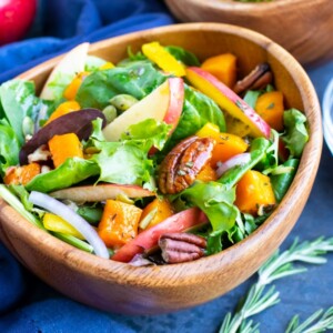 A wooden bowl full of a Fall harvest salad with apples, pecans, and an apple cider vinegar dressing.