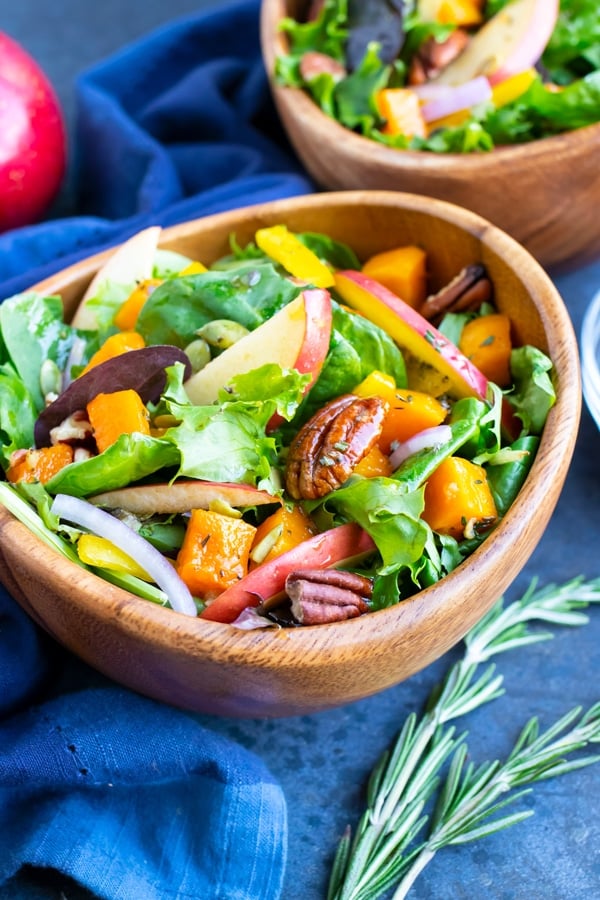 A wooden bowl full of a Fall harvest salad with apples, pecans, and an apple cider vinegar dressing.