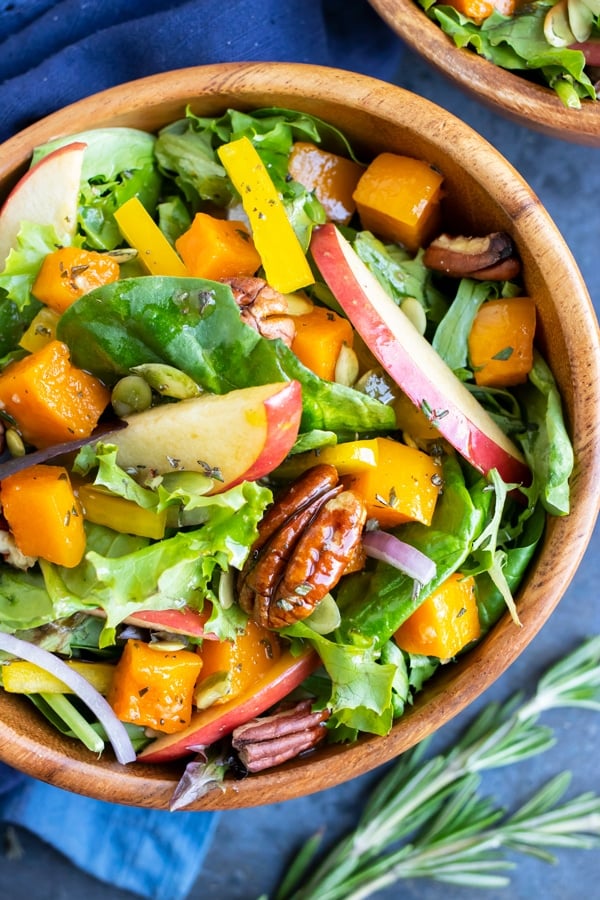 A close up of a salad bowl full of spinach, kale, toasted pecans, and apples.