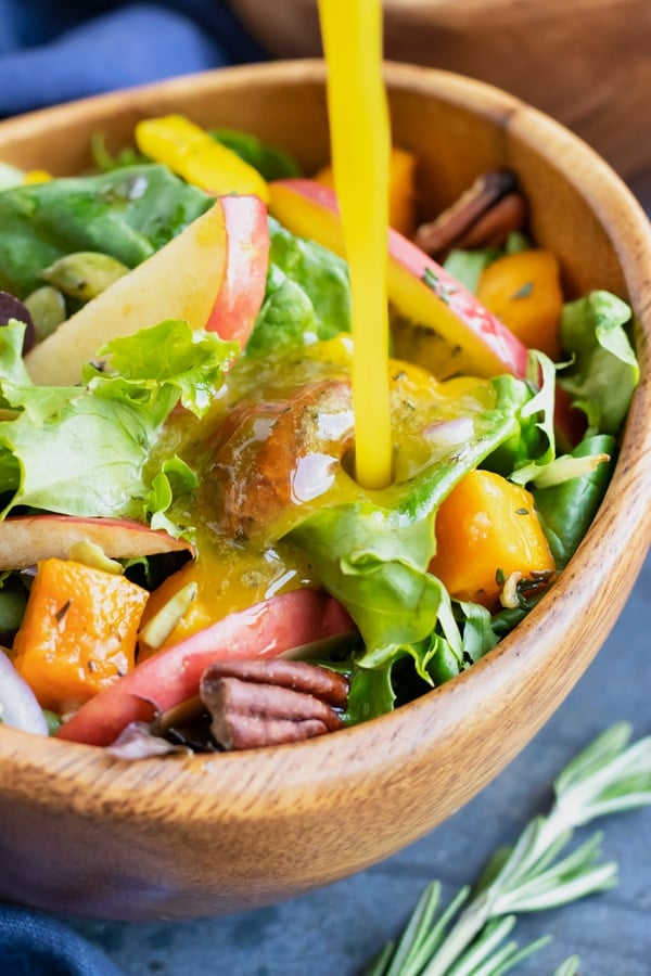 Apple cider vinegar salad dressing being poured onto a healthy Fall salad.