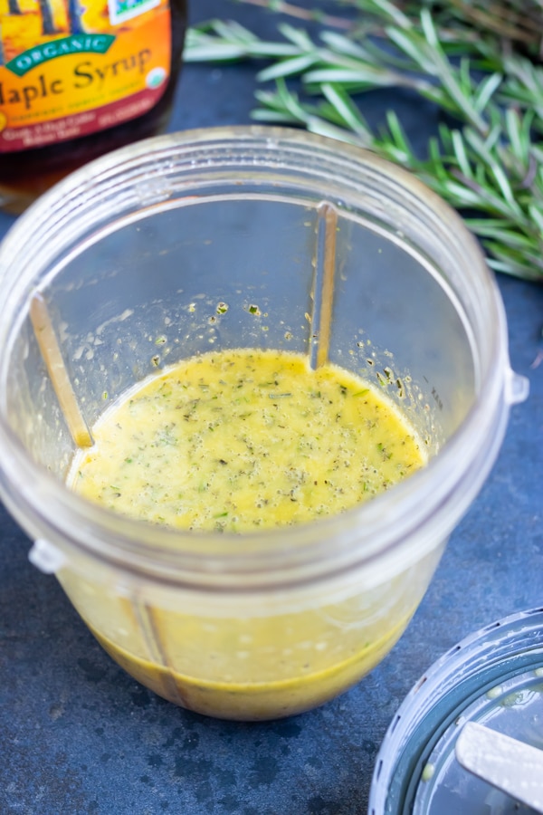 Apple cider vinegar salad dressing with maple syrup and rosemary in a clear cup.
