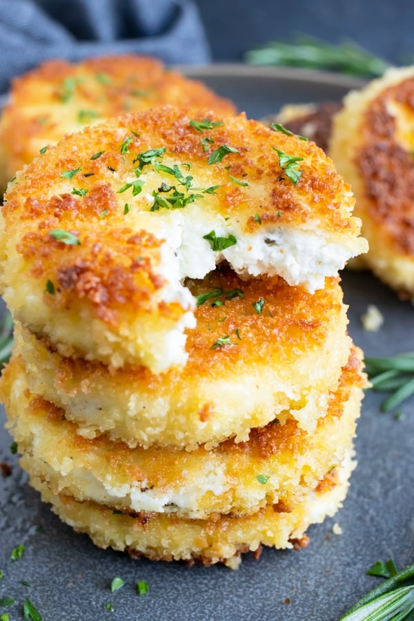 A stack of fried goat cheese slices with a bite taken out of one.